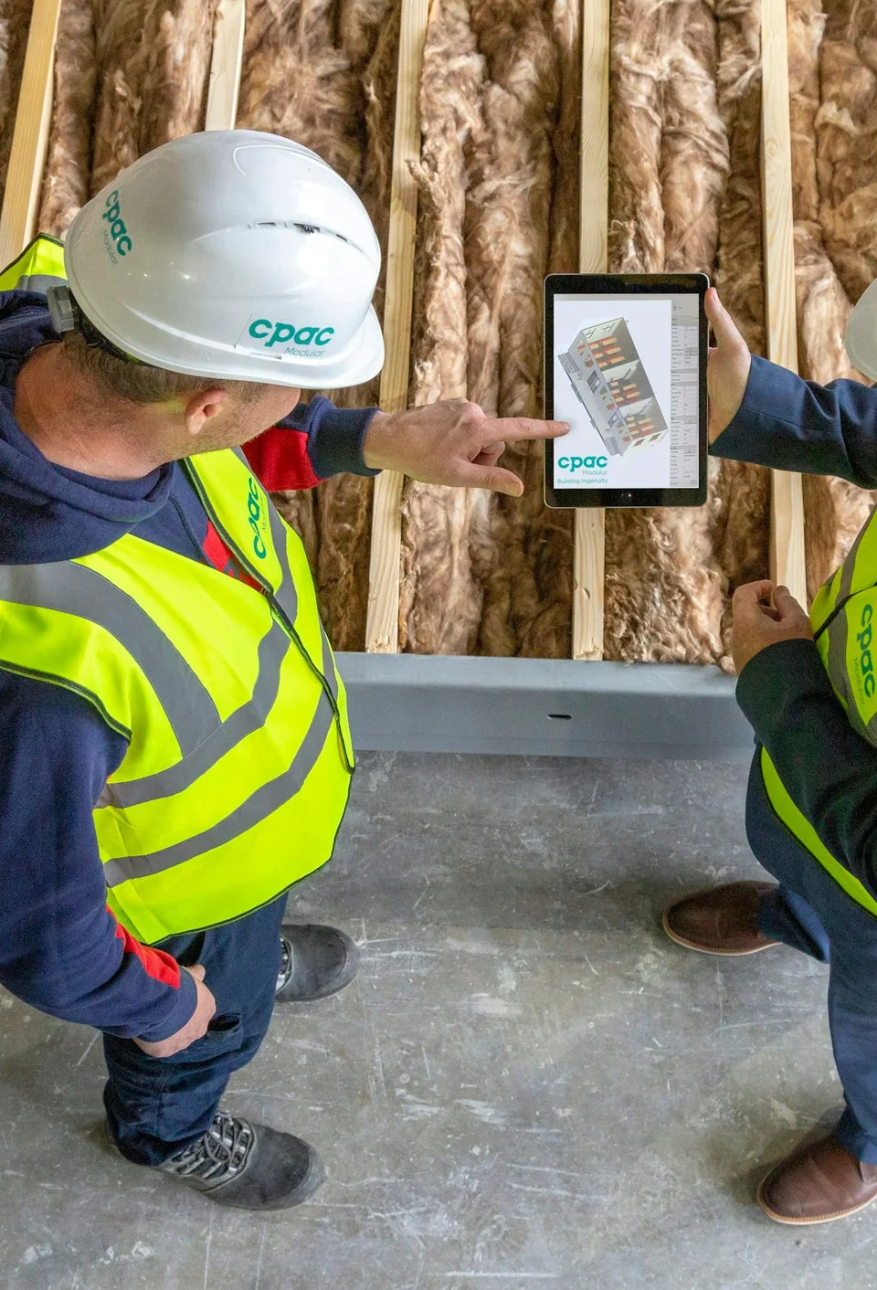 Two construction workers reviewing plans on a tablet on site