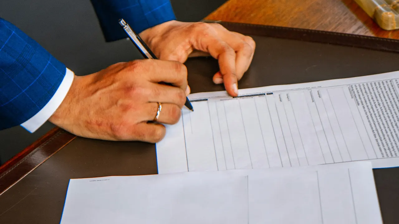 A person signing a printed agreement at a desk